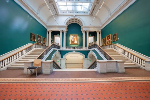 Large staircase in an art gallery with green walls and paintings. Symmetrical architecture,