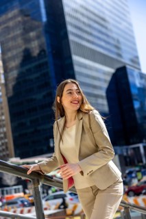 Professional woman in a neat suit is smiling, looking away with a hopeful expression while standing