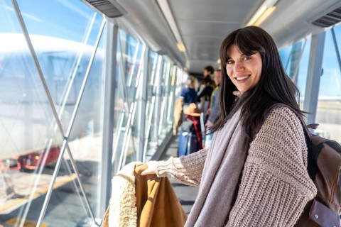 Young woman smiling, ready for travel and vacation, boarding an airplane through a jet bridge with