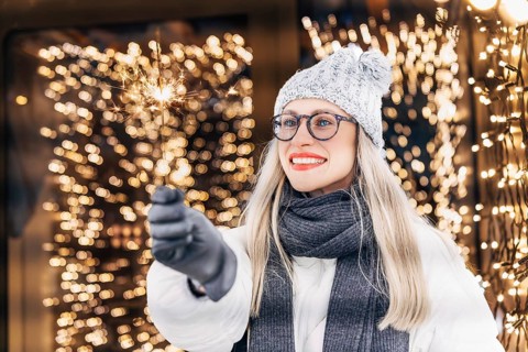 Young happy woman with a sparkler in her hand on the background of glowing garlands. A woman