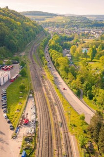 Railway line in mountainous area with forests, roads and cars in sunny weather, electrification of