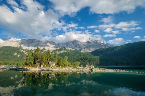 Symmetrical mountain reflection in the calm waters of Eibsee lake framed by green trees in the
