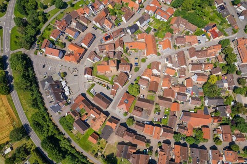 Aerial view of a village with houses close together with red roofs surrounded by green landscape,