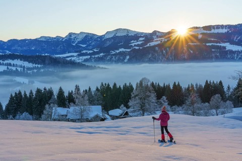 Landscape with woman watching sunrise over the Nagelfluh mountain chain during a snowshoe hike in