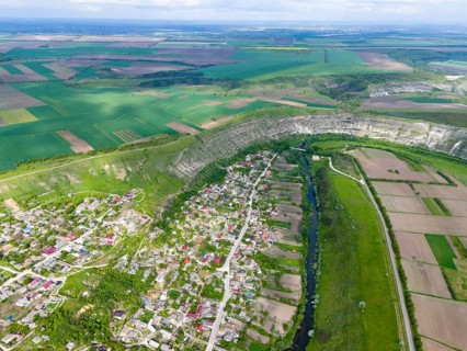 Village and agricultural fields surrounded by hills and a river in a green landscape, aerial view,