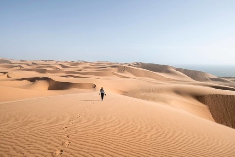 Woman with camera, lonely person walking across dunes, sand dunes with wave pattern, dune sea,