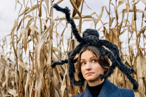 Portrait of a woman in a cornfield with a huge toy furry spider on her head. Halloween Party