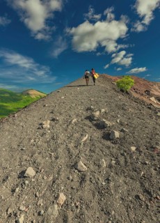 Rear view of two tourists climbing Cerro Negro with a beautiful landscape in the background.