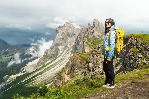 Happy female traveler yellow backpack stand on famous viewpoint ridge line Seceda South Tyrol