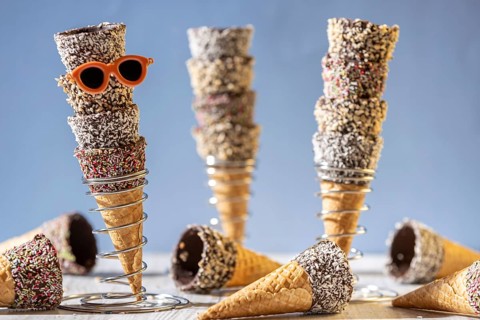 Ice cream cones stacked in metal stands, decorated with sprinkles, nuts and sunglasses