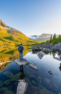 Young man standing on a rock in water, enjoying the landscape, picturesque mountain scenery in the
