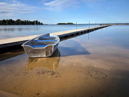 Lonely boat on a sandy beach next to a jetty. Blue sky and calm water surface, Vänern, Mellerud,