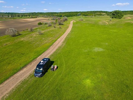 A camper stands next to a dirt road on a green field under a blue sky, aerial view, motorhome,