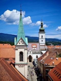 View from Lotrscak Tower, view of cathedral with a tall tower and colorful roof in the middle of a