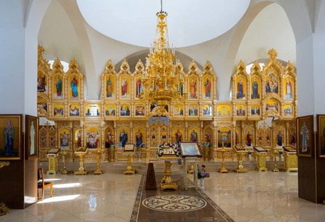 An extensive church room with richly decorated golden iconostasis and colorful religious paintings,