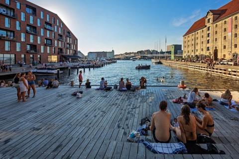 Menschen entspannen sich auf Holzplanken am Hafen bei sonnigem Wetter, Kopenhagen