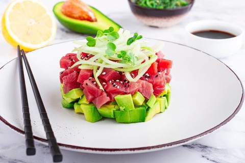 Fresh tuna tartare with avocado served on a marble table with soy sauce and seaweed salad
