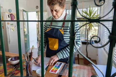 Viewed through green decorative iron bars, an older woman in a yellow-pocket apron selects colors