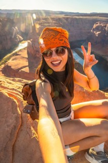 Young woman smiling and making a peace sign while taking a selfie on a rocky cliff overlooking the