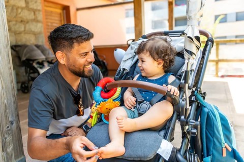 Cheerful father interacting with his smiling toddler son, who is sitting comfortably in a stroller