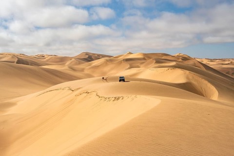 Off-road vehicle between sand dunes, sea of dunes, sandy desert, impressive desert landscape, Namib