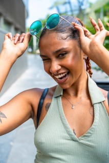 Young woman winking and smiling, confidently removing her mirror sunglasses from her head,