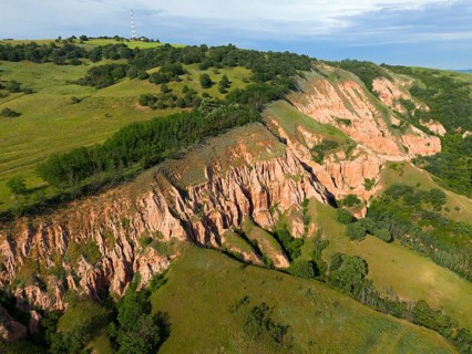 Red erosion rocks on grassy hills with thick vegetation and sky in the background, aerial view,