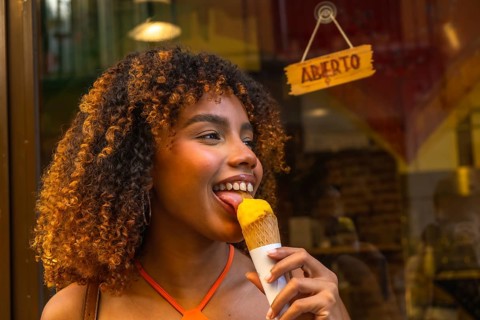 Young woman with beautiful curly hair smiling while licking a delicious scoop of yellow ice cream