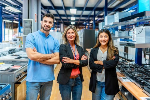 Diverse team of sales assistants and a manager smiling with arms crossed, standing between rows of