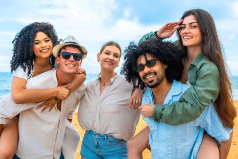 Diverse group of young adult friends smiling and having fun on a beach, with two women riding