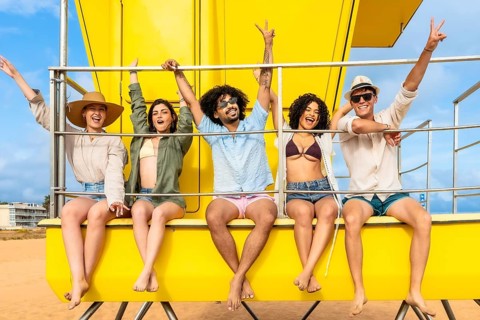 Group of diverse young people enjoying a joyful summer vacation on the beach, sitting cheerfully on