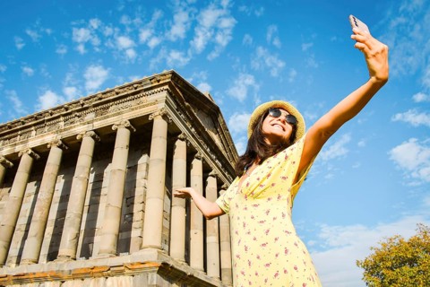 Happy female tourist takes a selfie photo against the background of the famous Garni Temple - one