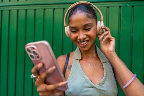 Young black woman with headphones smiling while looking at her smartphone, enjoying music and