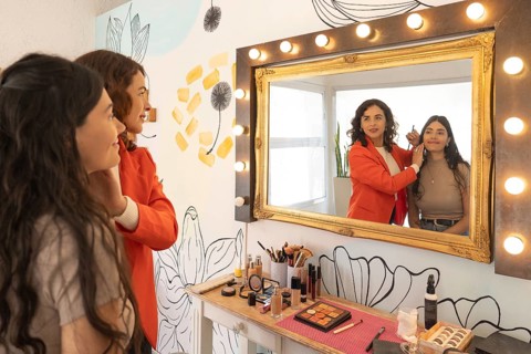 Reflection of a makeup artist and her client smiling together in a vanity mirror while checking the