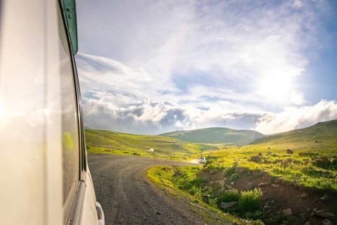White car drives on caucasian green wilderness with sky and meadow view. Tusheti. Georgia