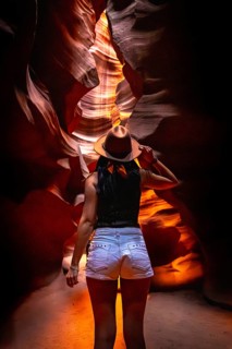 Woman in a hat walks through glowing sandstone walls of antelope canyon, exploring warm orange red