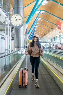 Young woman smiling while walking on a moving walkway in a modern airport terminal, carrying a pink