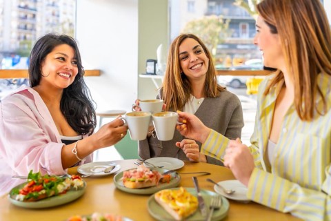 Three diverse women friends enjoying a delightful brunch together at a modern cafe, toasting coffee