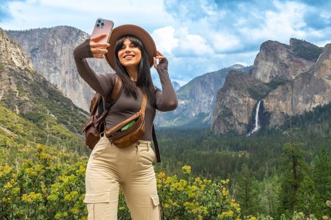 Woman standing at tunnel view in yosemite national park, holding a cell phone and taking a selfie
