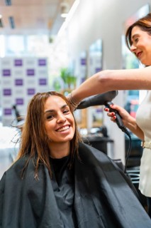 Smiling woman in salon chair receiving a professional blow dry from a hairstylist, enjoying