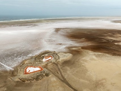 Saline ponds with ruddy algae growth and white salt deposits at the Atlantic Coast. Aerial view.