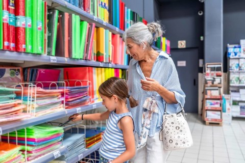 Grandmother and granddaughter shopping for stationery in a supermarket aisle, selecting colorful