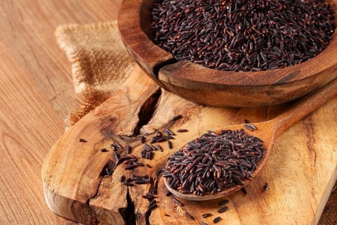 Natural black rice in a wooden bowl and spoon on a wooden surface in rustic style, top view