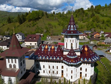 Combination of Orthodox church and surrounding village in hilly landscape under cloudy sky, aerial