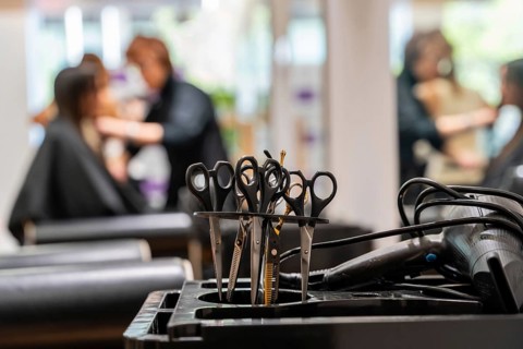 Professional hairdressing scissors and a blow dryer sitting on a salon cart, with a blurred