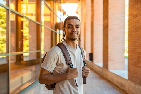 Young man wearing a backpack and casual attire, standing confidently on a university campus walkway