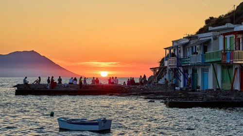 Sunset scene with coastal buildings, boat and people as silhouettes in front of the sea,