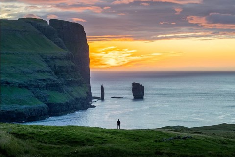 Person on a rock edge off the coast near Gjogv, Faroe Islands