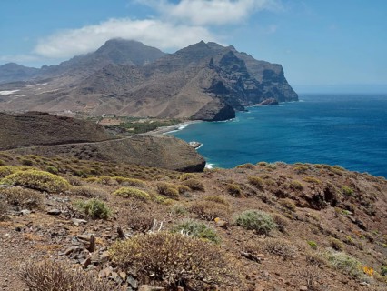 Rugged coastal landscape with hills and views of the blue sea under slightly cloudy sky, La Aldea