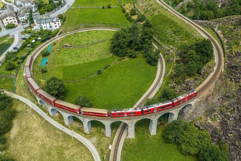 Red train of the Rhaetian railroad line, Bernina Express, passing the circular Brusio viaduct,